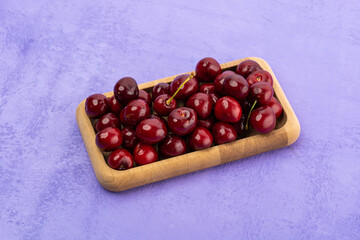 ripe red cherries in a wooden bowl on a purple background