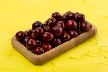 ripe red cherries in a wooden bowl on a yellow background
