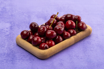 ripe red cherries in a wooden bowl on a purple background