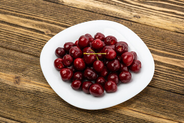 ripe red cherries in a white plate on a wooden background