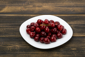 ripe red cherries in a white plate on a wooden background