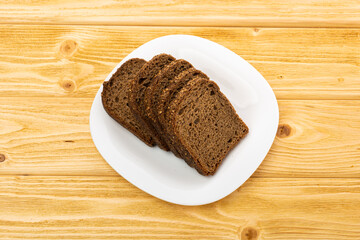 sliced rye bread in pieces in a white plate on a wooden background