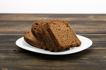 sliced rye bread in pieces in a white plate on a wooden background