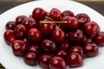 ripe red cherries in a white plate on a wooden background