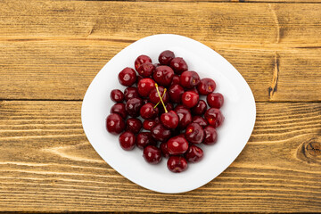 ripe red cherries in a white plate on a wooden background