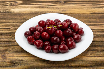 ripe red cherries in a white plate on a wooden background