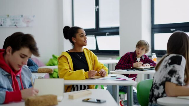 High school students paying attention in class, sitting in their desks and raising hand.