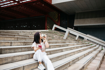 Young brunette woman sitting on stairs drinking coffee and using a phone