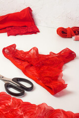 Red lace lingerie, female panties, tailor workplace equipment fabric, scissors, thread. Handmade underwear workshop