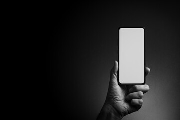 Man's hand holding smartphone with blank screen isolated on dark background