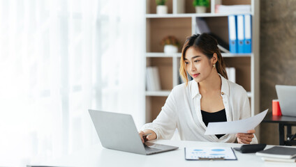 Beautiful young woman using laptop and smiling while working in office, business concept.