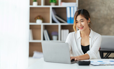 Fototapeta premium Beautiful young woman using laptop and smiling while working in office, business concept.