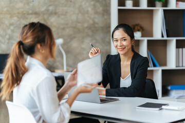 Two young business woman having a meeting in the office sitting at a desk having a discussion.