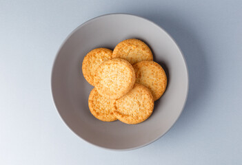 Minimalism. Yellow cookies in a gray plate on a gray background. Close-up. View from above. A place to copy.