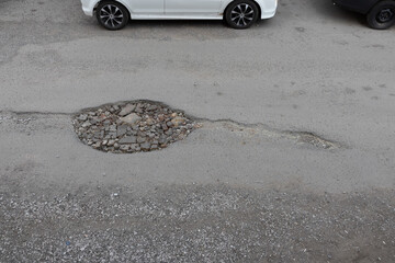 Close-up of pit on the road with crack similar to spermatozoon. Repair of the asphalt carriageway with broken bricks and scrap cement tiles - obrazy, fototapety, plakaty