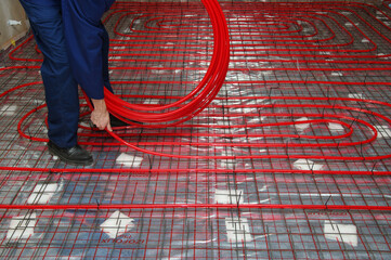 Worker is installing a red pipe for underfloor heating