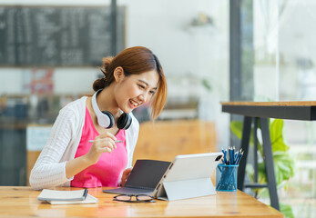 Attractive office worker writing in notepad placed on bright desktop, Female student taking notes from a book at library. Young asian woman sitting at table doing assignments in college library.