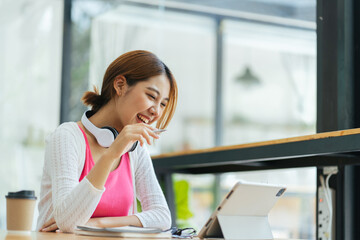 Obraz premium Young adult happy smiling Asian student wearing headphones talking on online chat meeting using laptop in university campus or at virtual office. College female student learning remotely.