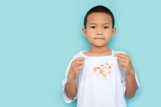 Asian Kid Showing Dirty Sauce Or Food Stain On Shirt From Eating In Meal. Dirty Stain For Cleaning Concept.