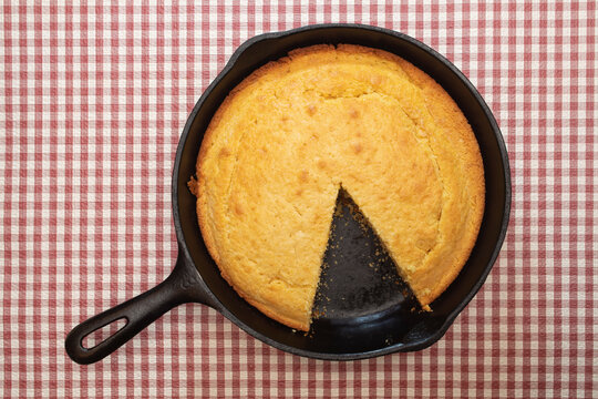 Cornbread in a cast iron skillet sitting on a red and white checkered tablecloth