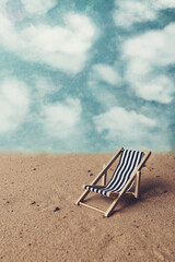 View of a blue and white deck chair on sand. Blue sky background with white fluffy clouds