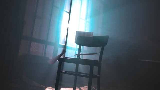 Aged book pages falling on black chair in rays of bright light shining through window shutters in old mansion. Volume of a rare book edition in an archive filled with haze. Mystic dark library room.