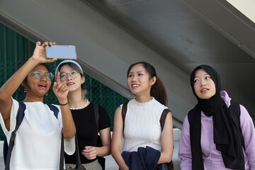 Four group young attractive Asian multi ethnic woman friends colleagues students talk walk discuss mingle outdoors backpack handphone photo