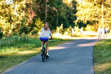 A young woman riding a bicycle in a park in summer in the sunny morning.