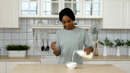 African American girl in slow motion stirs crispy muesli with milk in a bowl. Healthy quick...