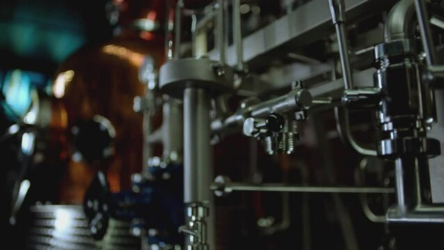 Camera moving across metallic tubes inside alcohol drinks factory. Wine , vodka cognac distilling tanks . Metal taps or kegs for pouring alcohol . slow motion close-up . Row of chrome pipes in factory