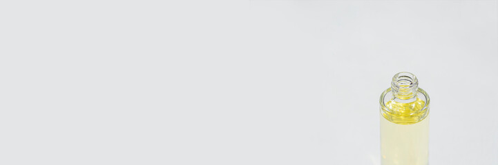 Open transparent bottle without cap with serum or essential oil with in soft focus. White background with daylight and beautiful shadows. Beauty concept for face and body care