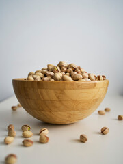 Bowl of pistachio nuts on the table. White background, wooden bowl