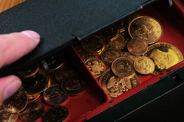 Ein Haufen Goldmünzen wird unter dem Deckel einer halb geöffneten Geldkassette sichtbar.