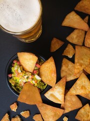 Bowl con guacamole, nachos y una cerveza en un fondo negro. Comida mexicana. Concepto de bebidas y...