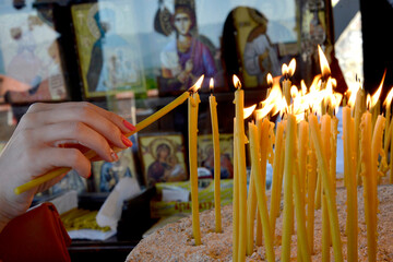Woman lighting an ortohodx church candle - obrazy, fototapety, plakaty