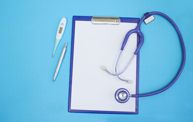 Stethoscope, tablet, pen and electric thermometer on a blue background. Copy space.