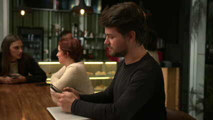 Young man doing his work inside coffee shop studying or working in front of laptop computer. People inside cafe