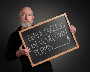 define success in your own terms - inspirational advice, senior male teacher or mentor with a blackboard sign, business, career, lifestyle and priorities concept