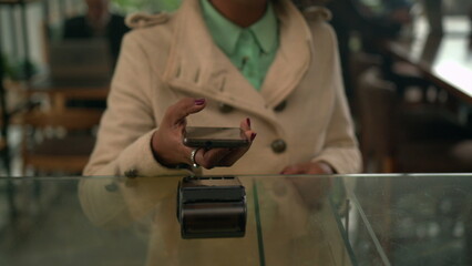 One black female customer paying with cellphone at counter. NFC payment with smartphone device at coffee shop