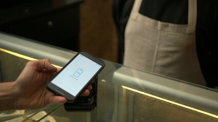 Customer paying with contactless NFC payment technology on smartphone device inside business store