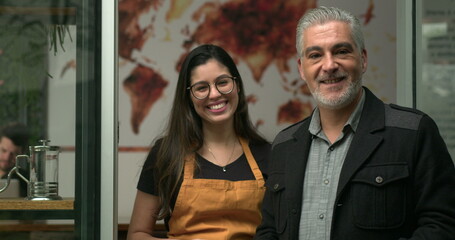 Male manager entrepreneur posing to camera with young female employee in front of coffee shop