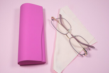 Pink frame womens glasses with glasses cleaning cloth and case on a pink background.