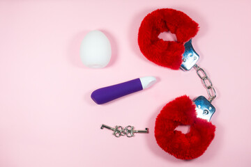 Red sexy fluffy handcuffs with keys and vibrator on a pink background. Erotic sex game with sexual...