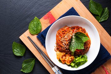 Food concept korean spicy cold buckwheat noodle Kimchi Bibim Guksu on wooden board and black background with copy space