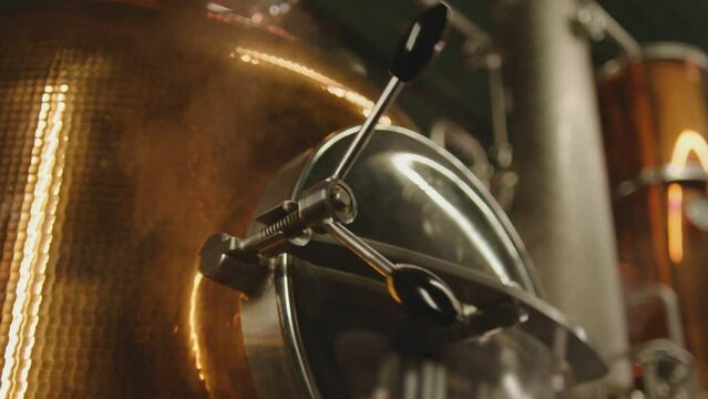 Professional big factory of alcohol drinks . Man's hand opening door of tank . Vodka wine tequilla production filtration , distillation . Alcohol preparation . Close up making alcohol . Boiler , steam