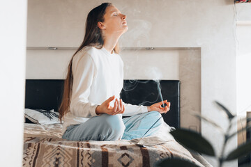 Woman Sitting On Bed At Home Meditating after waking up in morning sunrise, natural light. Zen,...