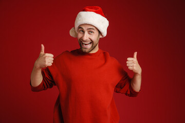 Fototapeta na wymiar Young white man wearing santa hat smiling and showing thumbs up