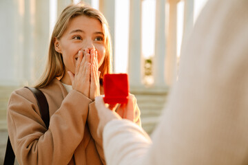 White man proposing to his excited girlfriend in park