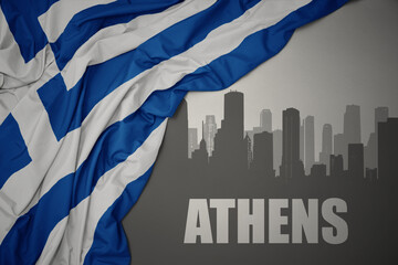 abstract silhouette of the city with text Athens near waving national flag of greece on a gray...