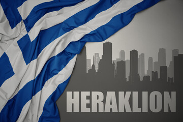 abstract silhouette of the city with text Heraklion near waving national flag of greece on a gray...